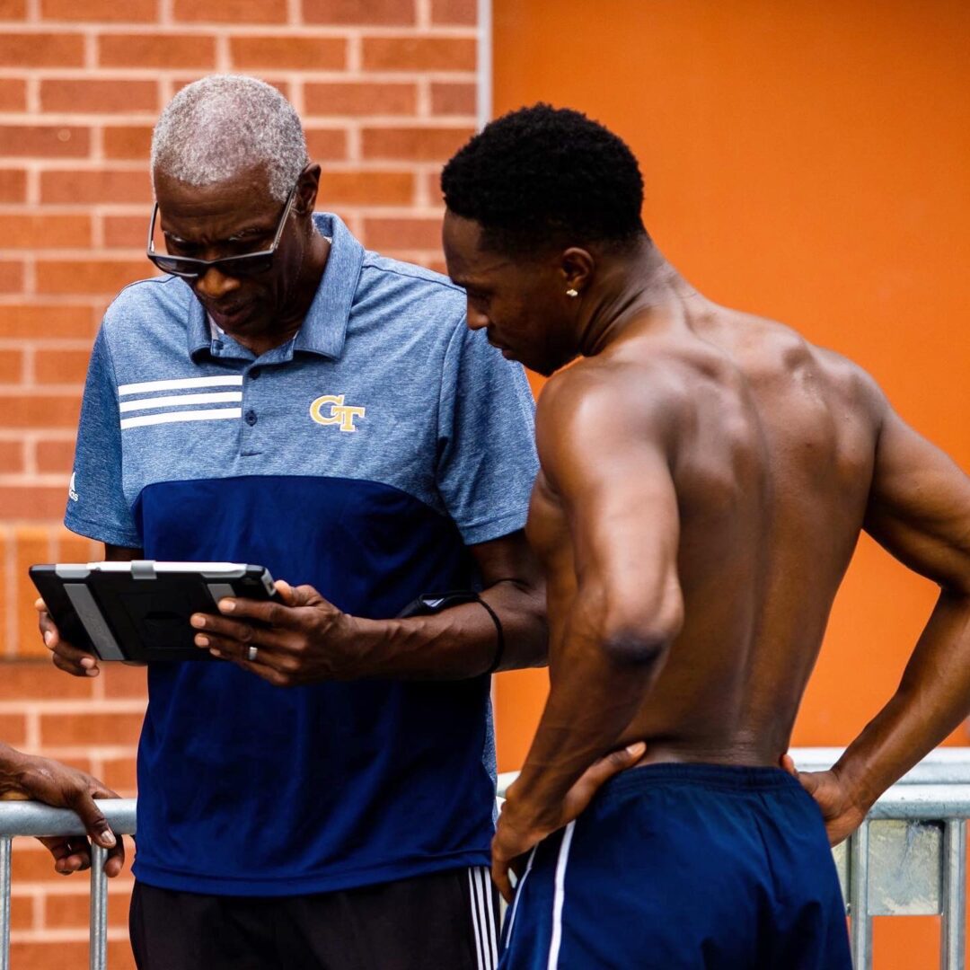 A man standing next to another man holding a tablet.