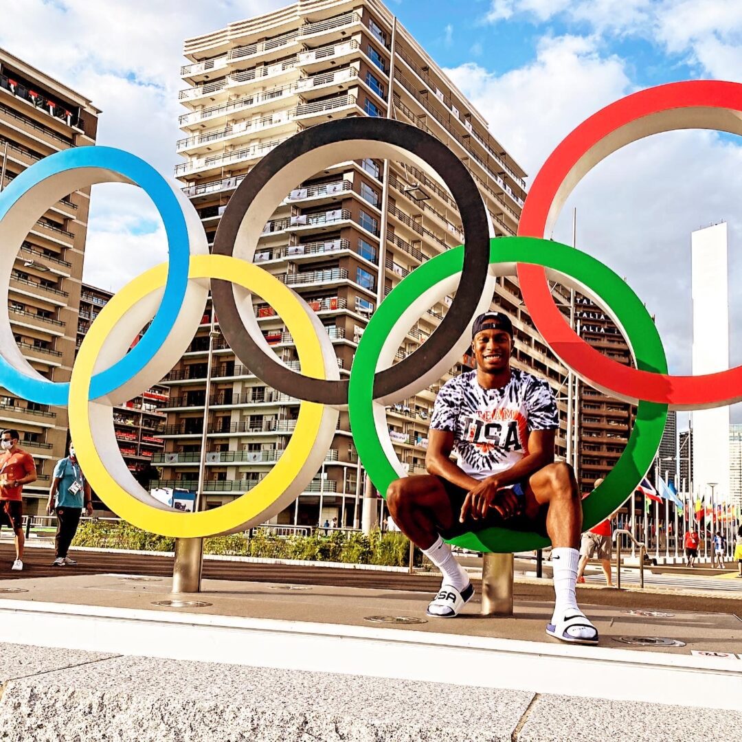 A man sitting on the ground in front of olympic rings.